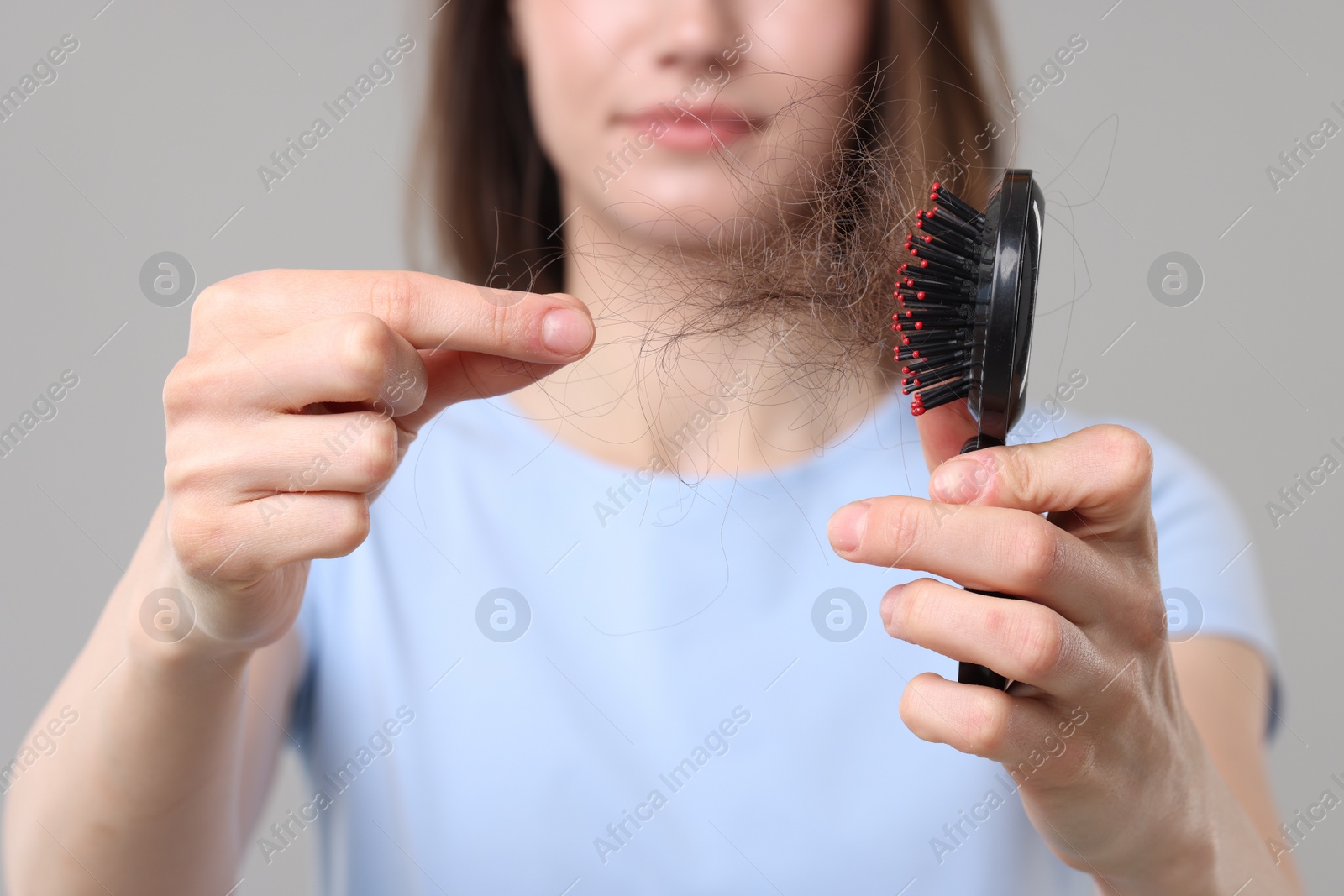 Photo of Woman taking her lost hair from brush on grey background, closeup. Alopecia problem