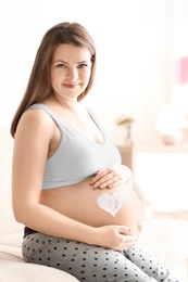 Pregnant woman with heart painted on her belly against blurred background