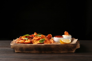 Photo of Tray with sweet potato chips and sauce on table against black background. Space for text