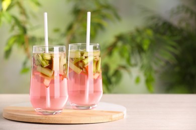 Glasses of tasty rhubarb cocktail on wooden table outdoors, space for text