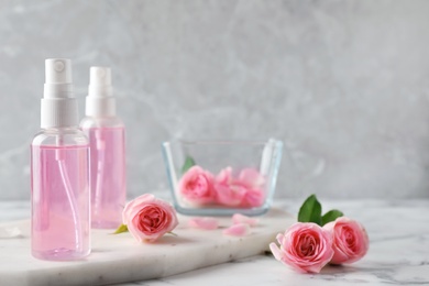 Bottles with rose essential oil and flowers on marble table, space for text