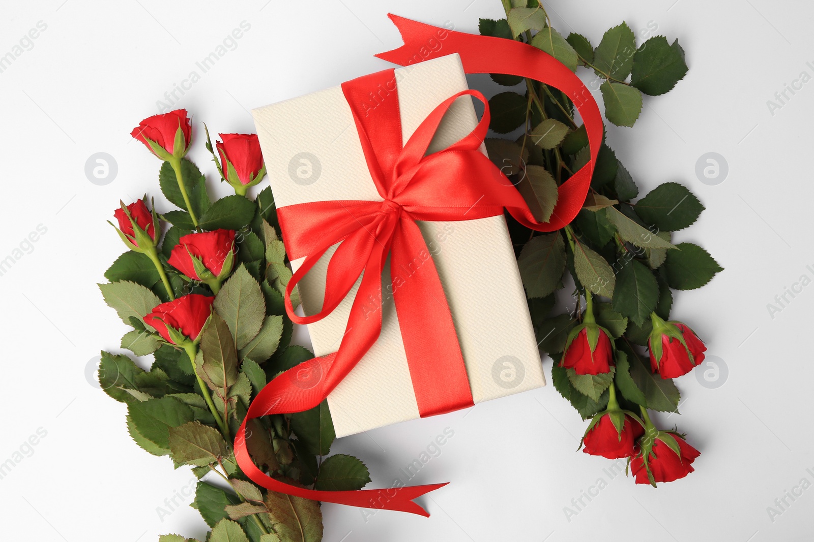 Photo of Beautiful gift box with bow and red roses on white background, flat lay