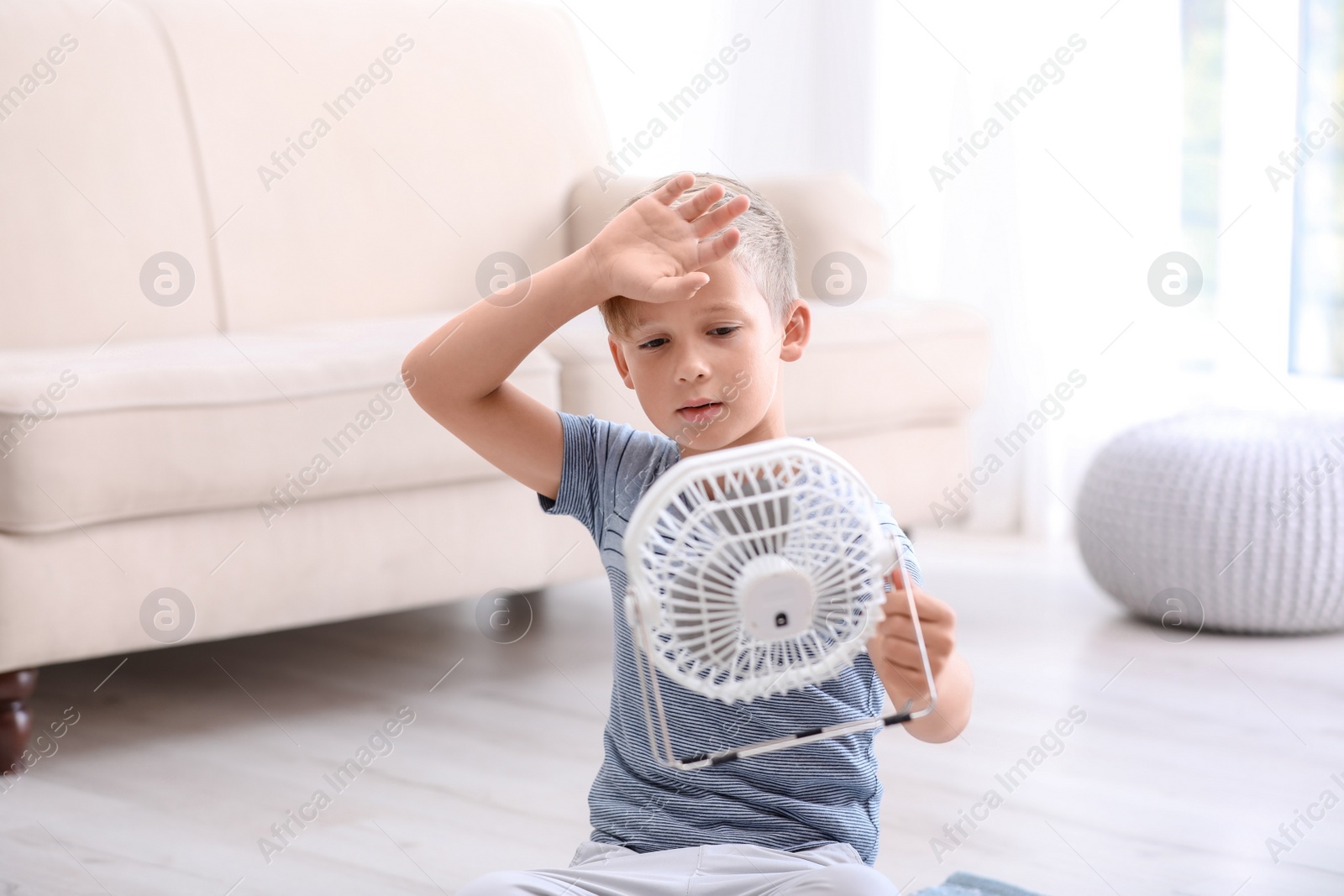 Photo of Little boy suffering from heat in front of fan at home