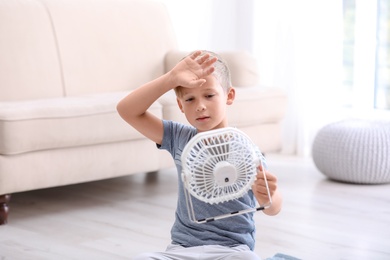 Little boy suffering from heat in front of fan at home
