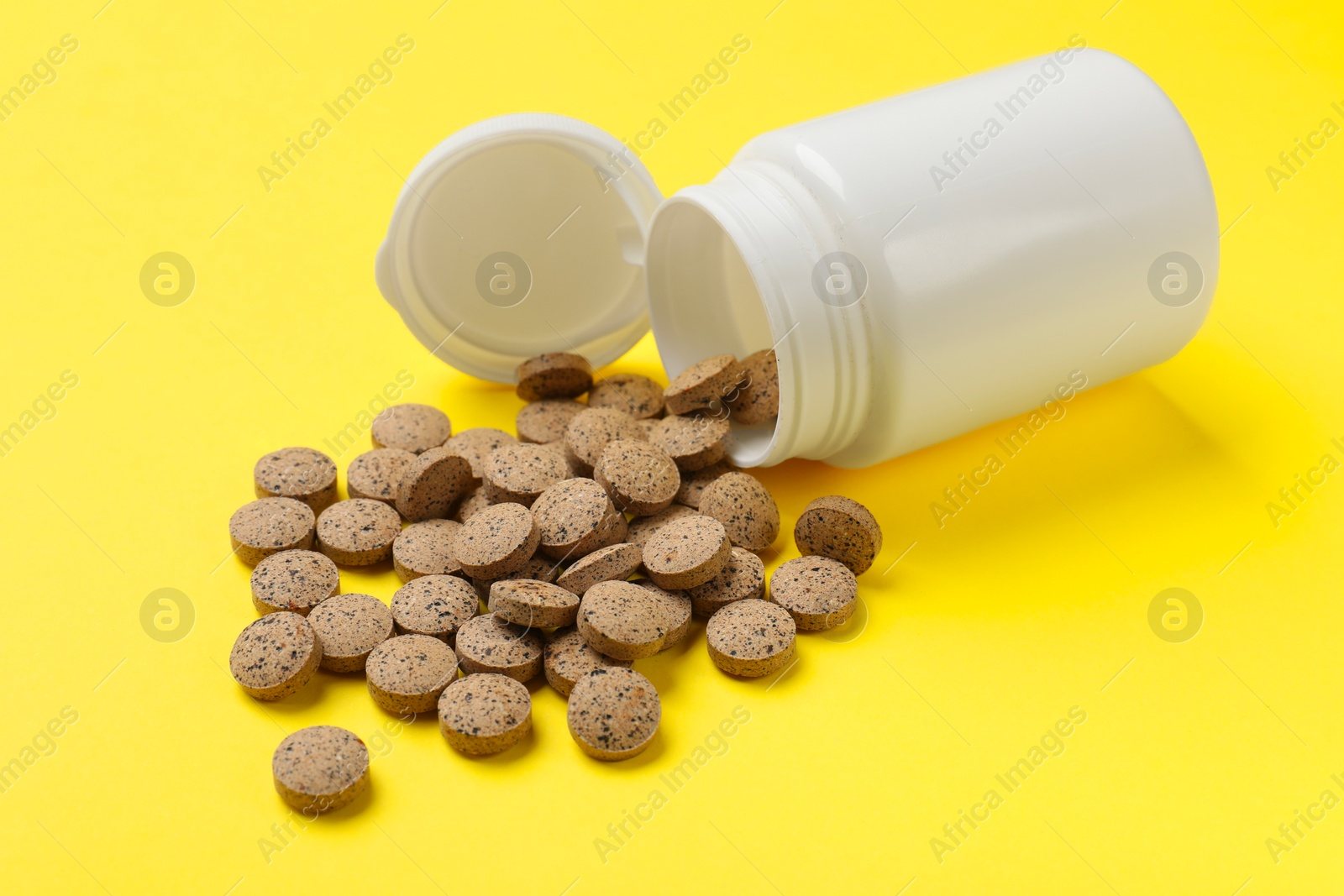 Photo of Vitamin pills and bottle on yellow background