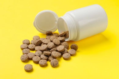 Photo of Vitamin pills and bottle on yellow background