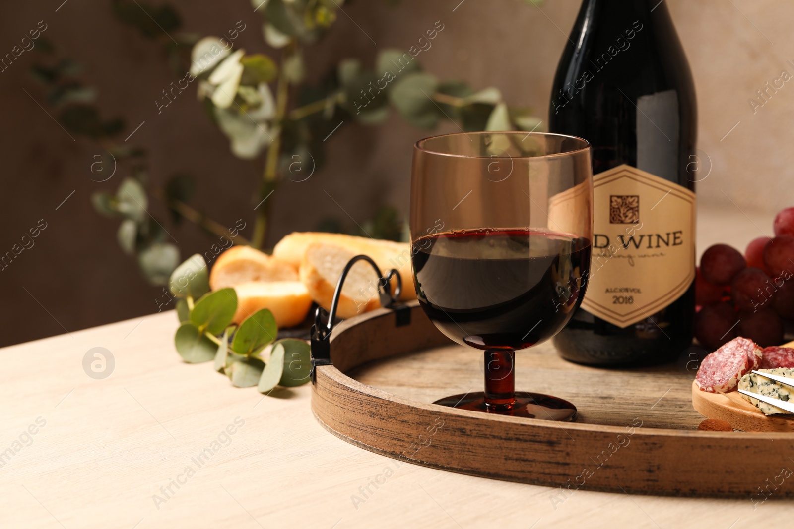 Photo of Glass of tasty red wine near bottle and delicious snacks on wooden table