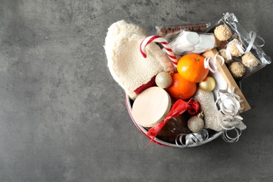 Basket with gift set and Christmas decor on grey table, top view. Space for text