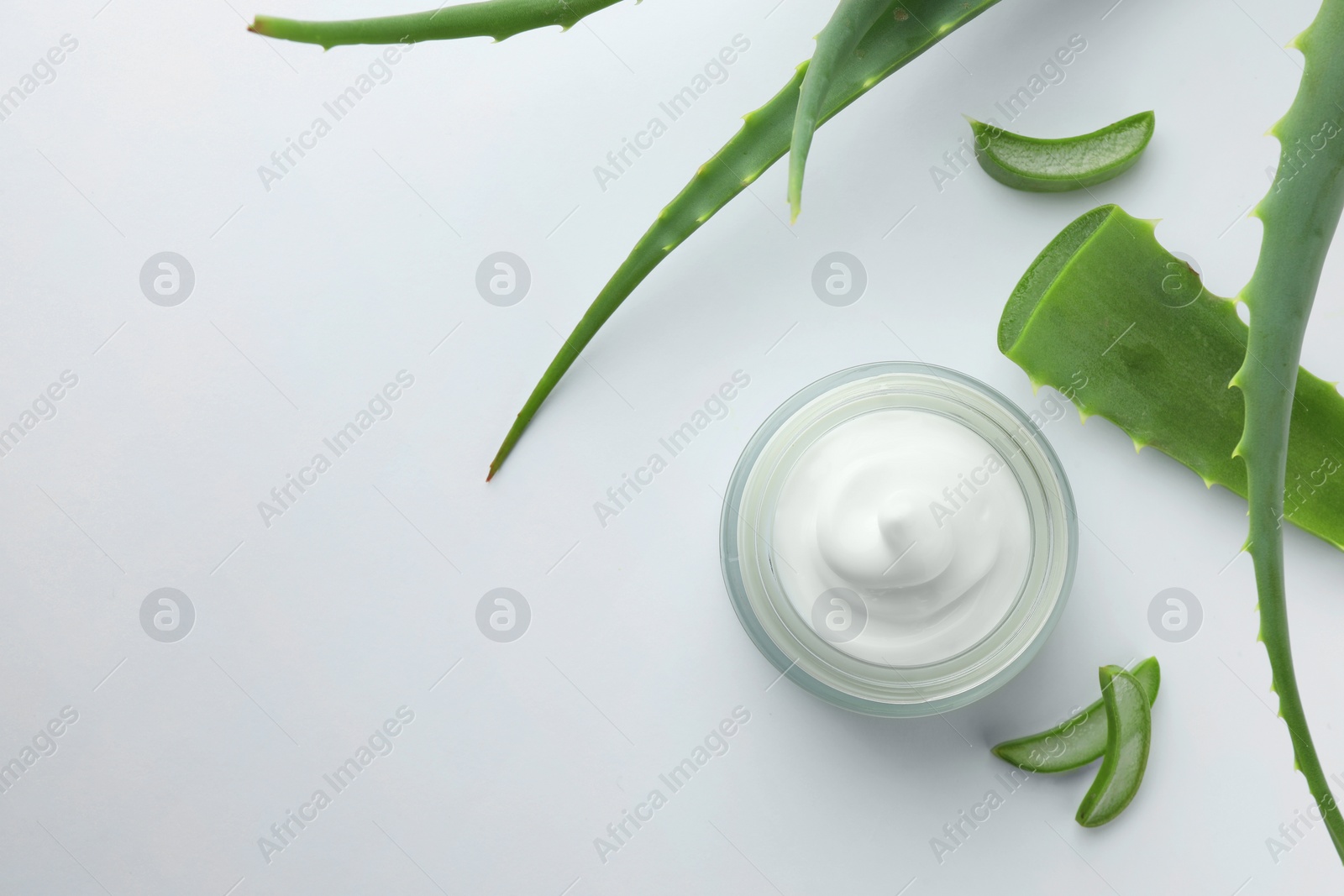 Photo of Jar of natural cream and aloe leaves on white background, flat lay. Space for text