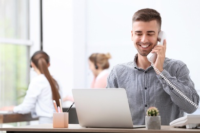 Male receptionist talking on phone at desk in office