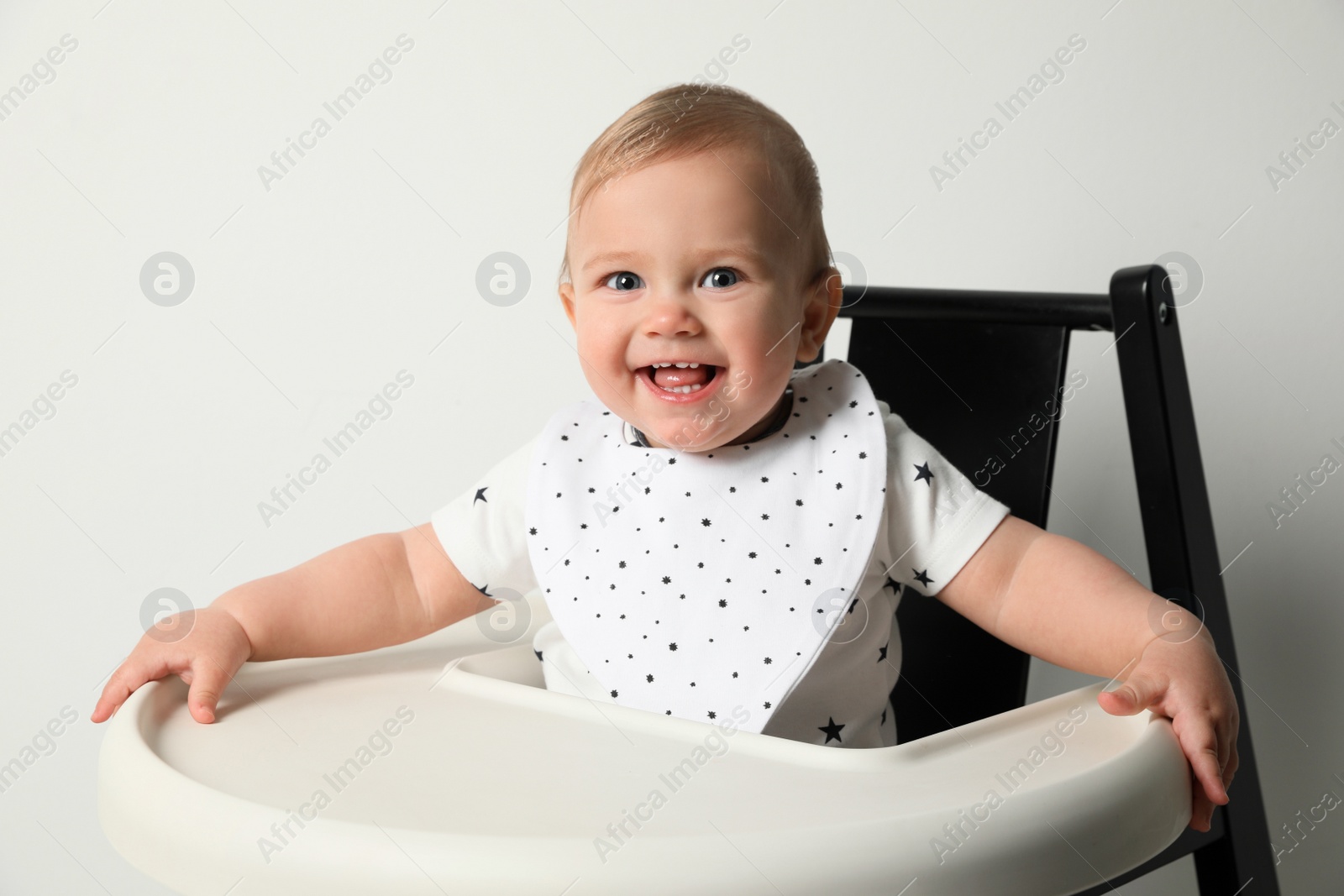 Photo of Cute little baby wearing bib in highchair on white background