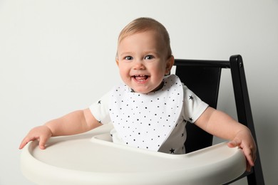 Cute little baby wearing bib in highchair on white background