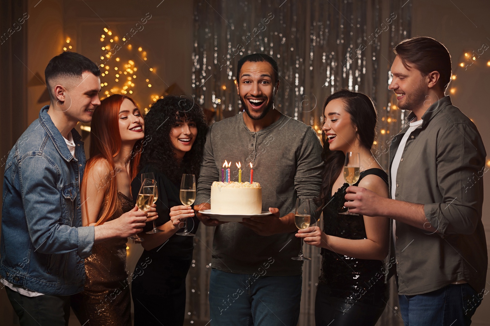 Photo of Happy friends with tasty cake and glasses of sparkling wine celebrating birthday indoors