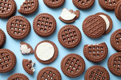 Photo of Tasty chocolate sandwich cookies with cream on light blue background, flat lay