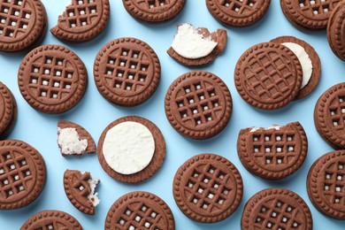 Tasty chocolate sandwich cookies with cream on light blue background, flat lay