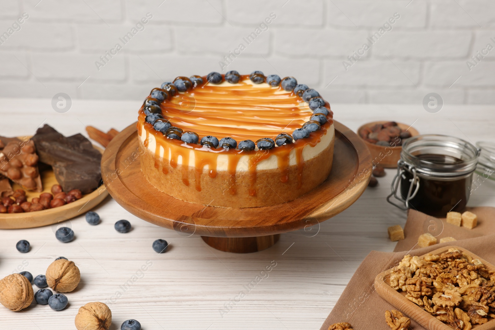 Photo of Delicious cheesecake with caramel and blueberries on white wooden table near brick wall