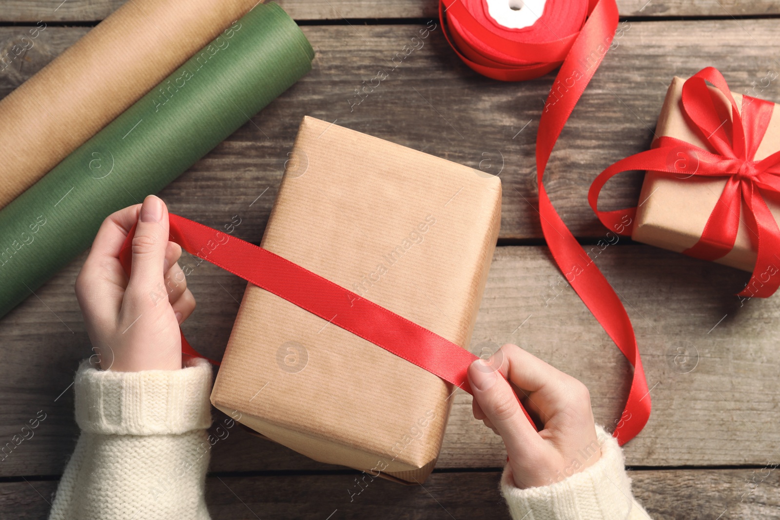 Photo of Christmas present. Woman tying ribbon around gift box at wooden table, top view