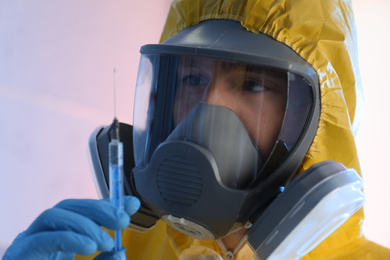 Photo of Scientist in chemical protective suit with syringe on color background, closeup