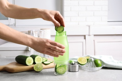 Photo of Young woman putting fresh cucumber slices into sports bottle on table. Space for text