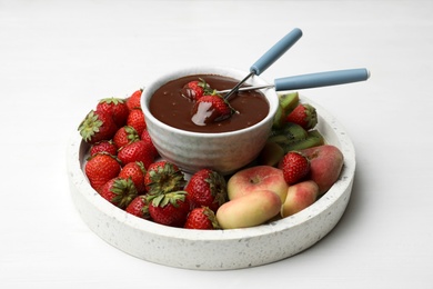 Photo of Fondue pot with chocolate and mix of fruits on white wooden table