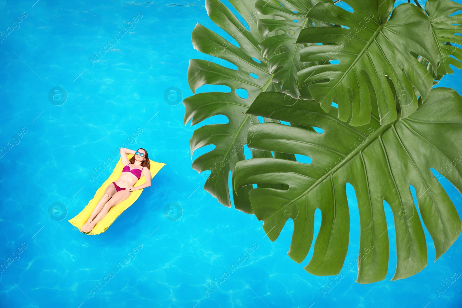 Image of View of beautiful green monstera leaves and young woman on inflatable mattress in swimming pool, above view