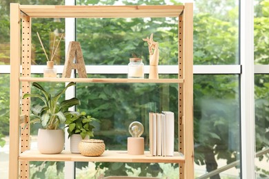 Photo of Wooden shelving unit with beautiful houseplants, books and air reed freshener indoors