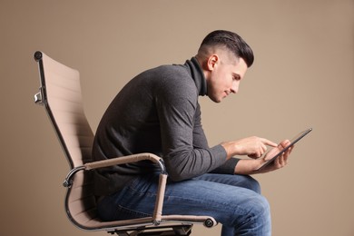 Photo of Man with poor posture using tablet while sitting on chair against beige background