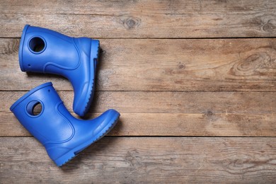 Photo of Blue rubber boots on wooden background, top view. Space for text