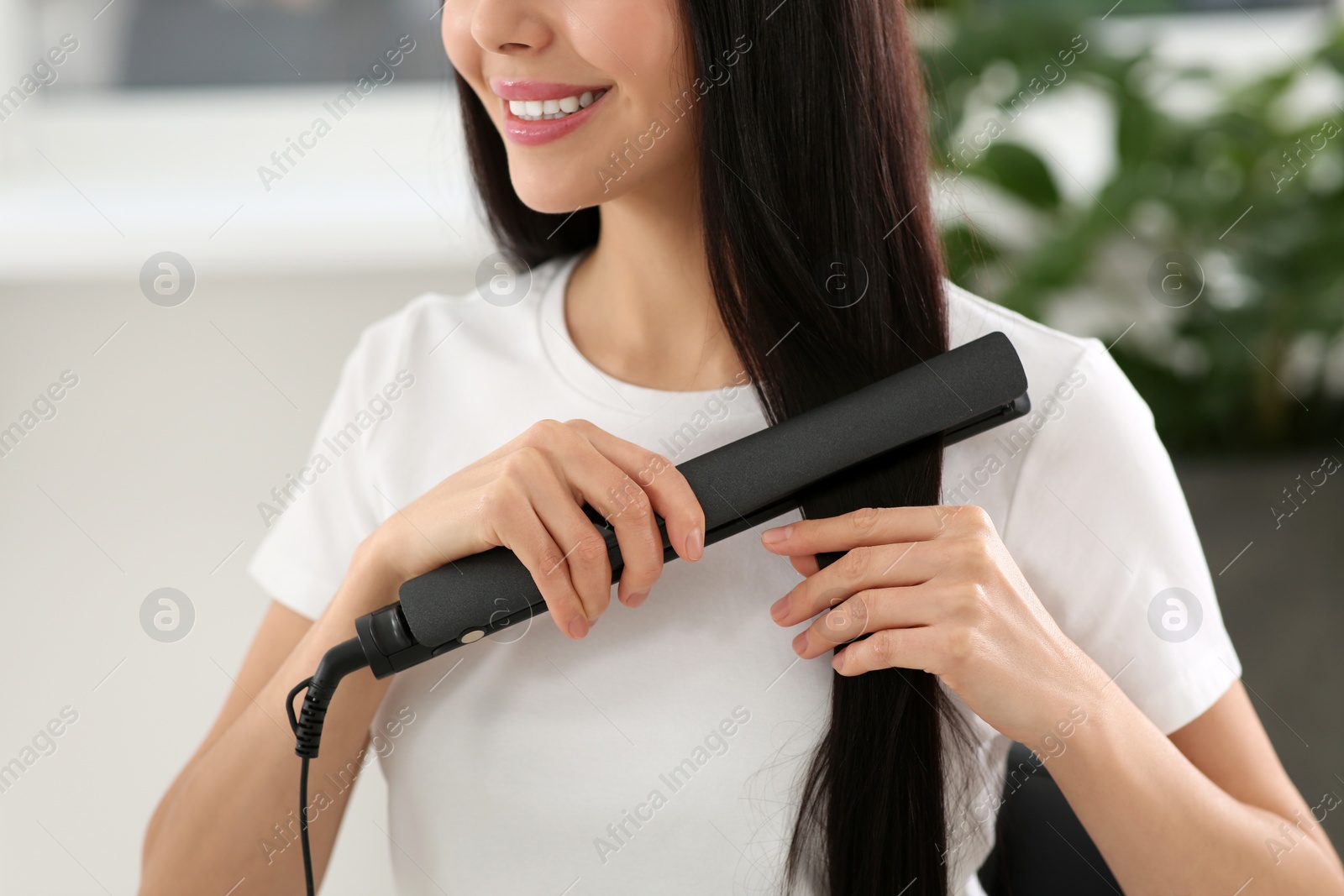 Photo of Happy woman using hair iron in room, closeup