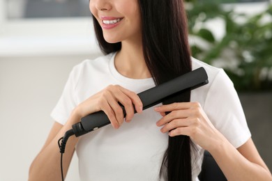 Happy woman using hair iron in room, closeup