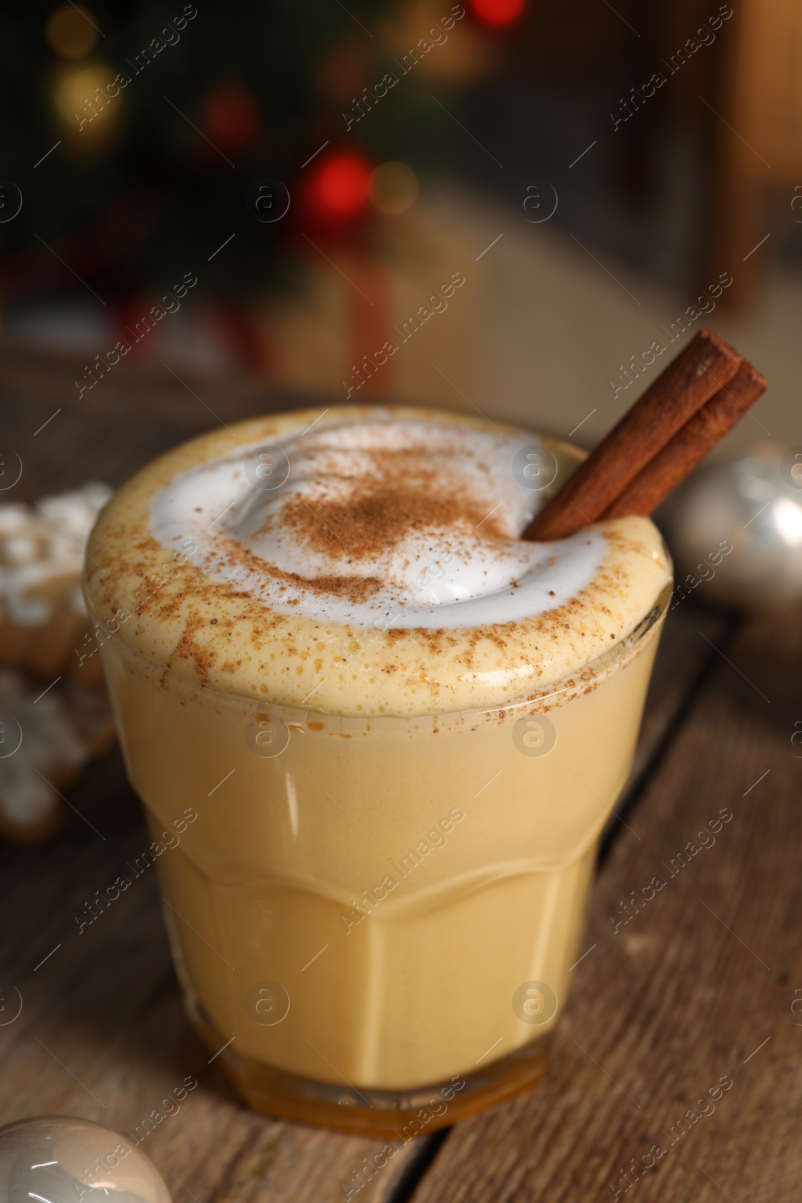 Photo of Tasty eggnog with cinnamon on wooden table against blurred festive lights, closeup