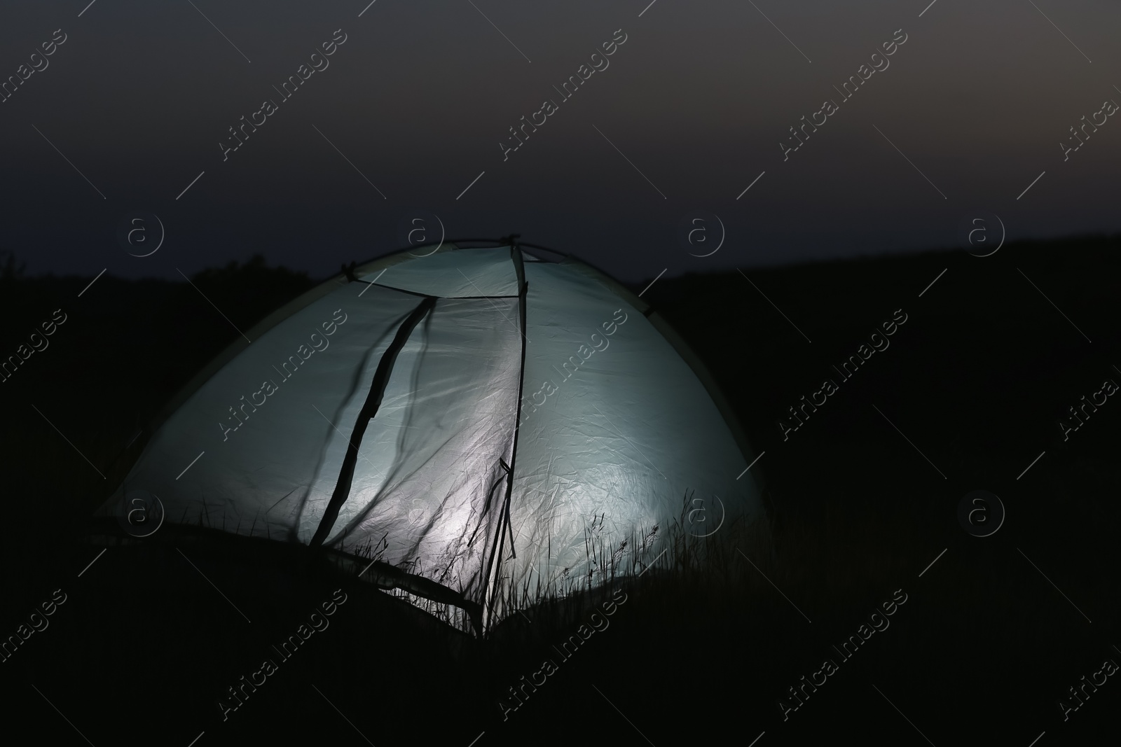 Photo of Modern tent lit from inside in wilderness at night, space for text. Overnight camping