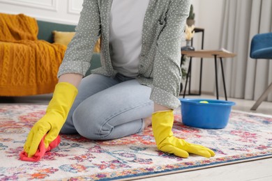 Photo of Woman in rubber gloves cleaning carpet with rag indoors, closeup