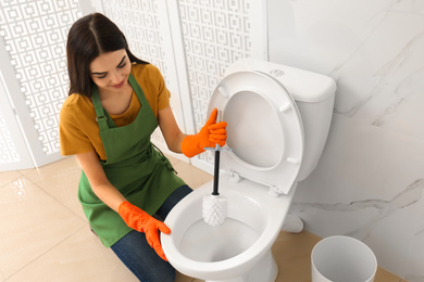 Young woman cleaning toilet bowl in bathroom