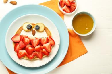 Photo of Creative serving for kids. Plate with cute owl made of pancakes, strawberries, cream, banana and almond on white wooden table, flat lay