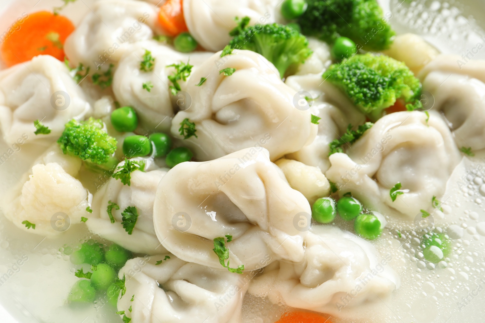 Photo of Tasty dumplings and vegetables in broth, closeup