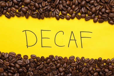 Photo of Word Decaf and coffee beans on yellow background, flat lay
