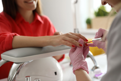 Photo of Professional manicurist applying polish on client's nails in beauty salon, closeup