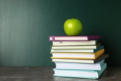 Photo of Books and apple on grey table near chalkboard, space for text. School education