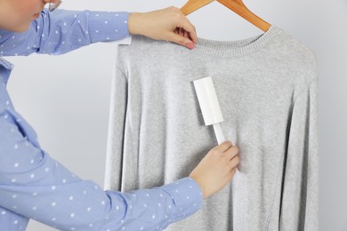 Woman cleaning clothes with lint roller on light grey background, closeup