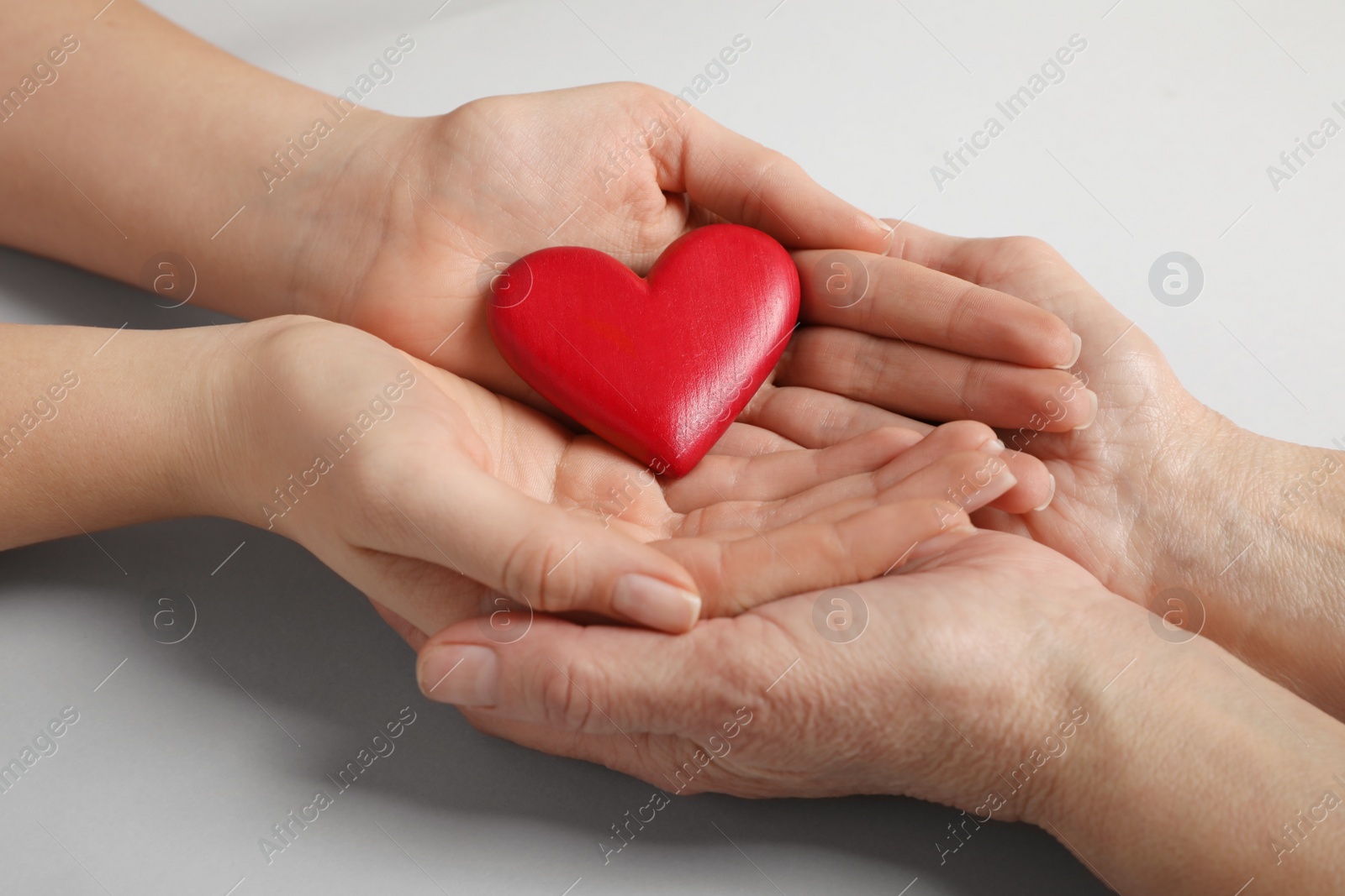 Photo of Young and elderly women holding red heart on light grey background, closeup