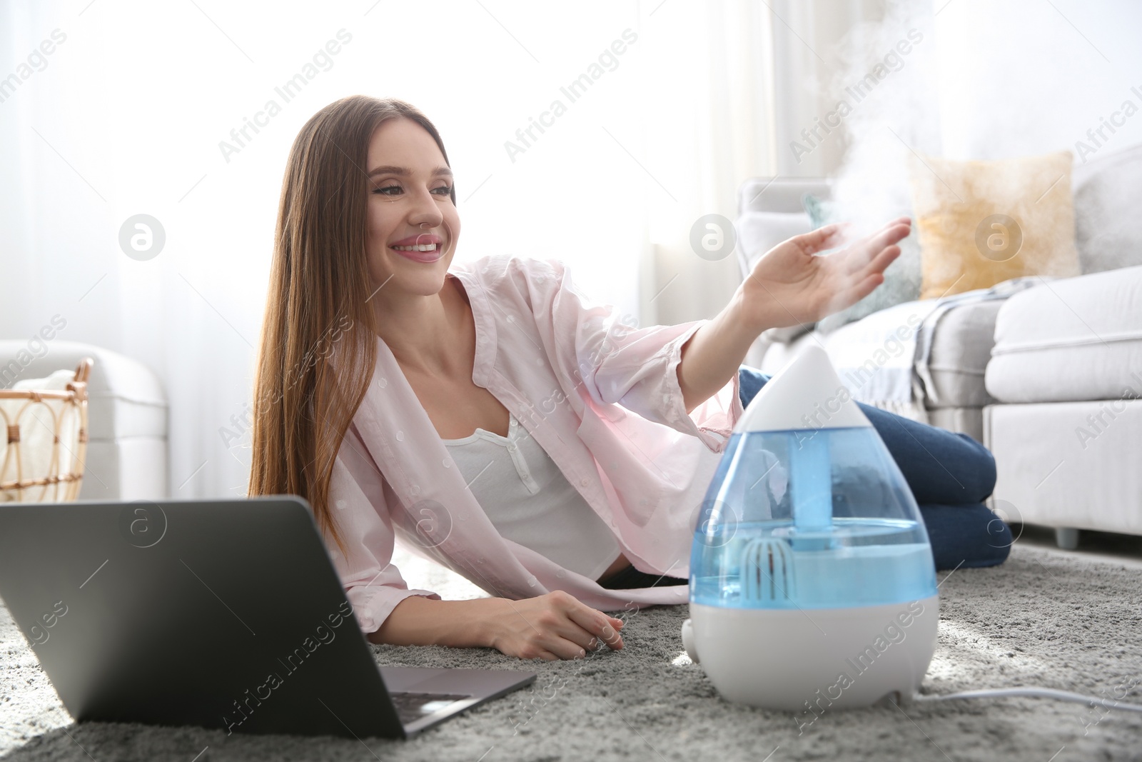Photo of Woman with laptop near modern air humidifier at home