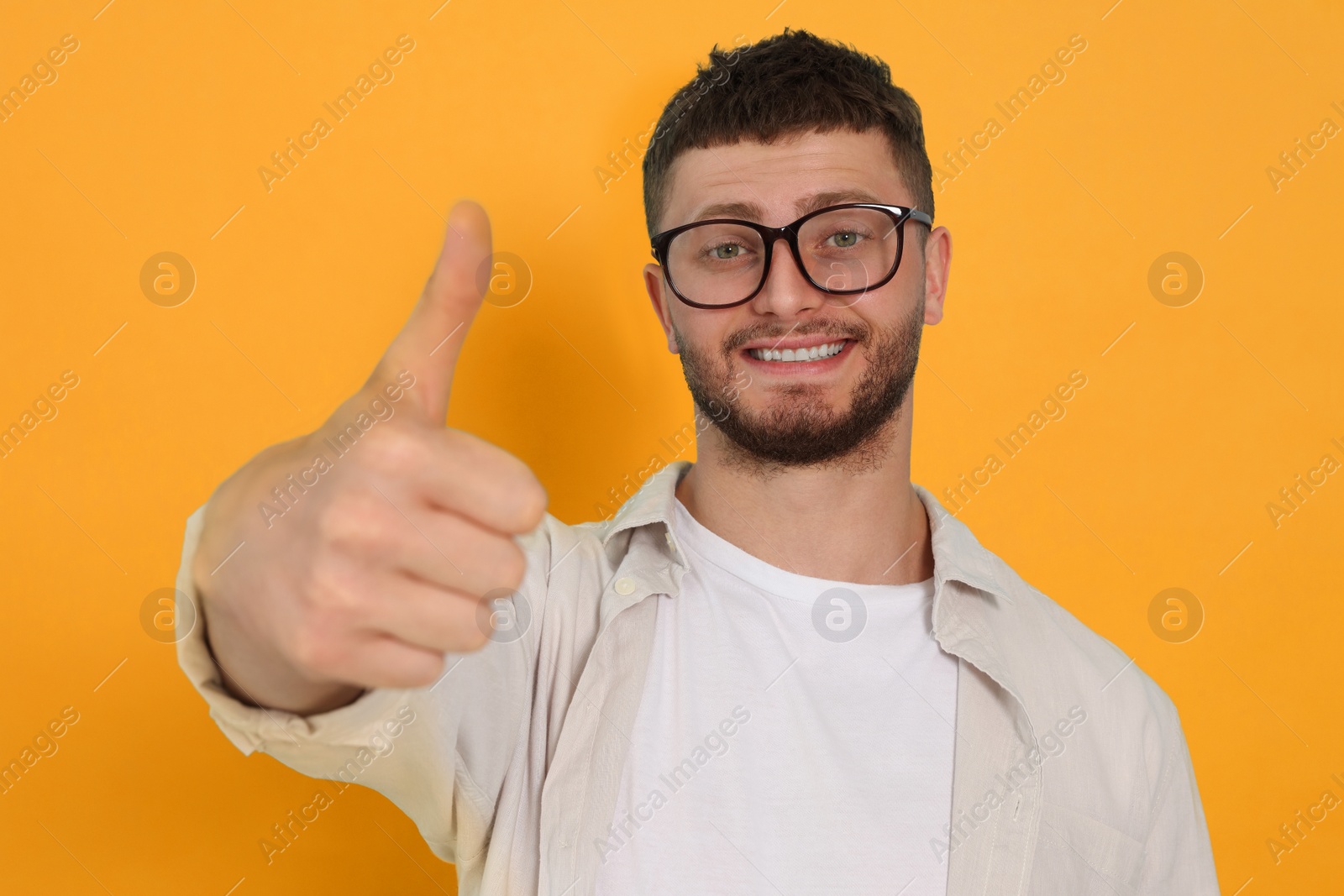 Image of Young man showing thumbs up on orange background