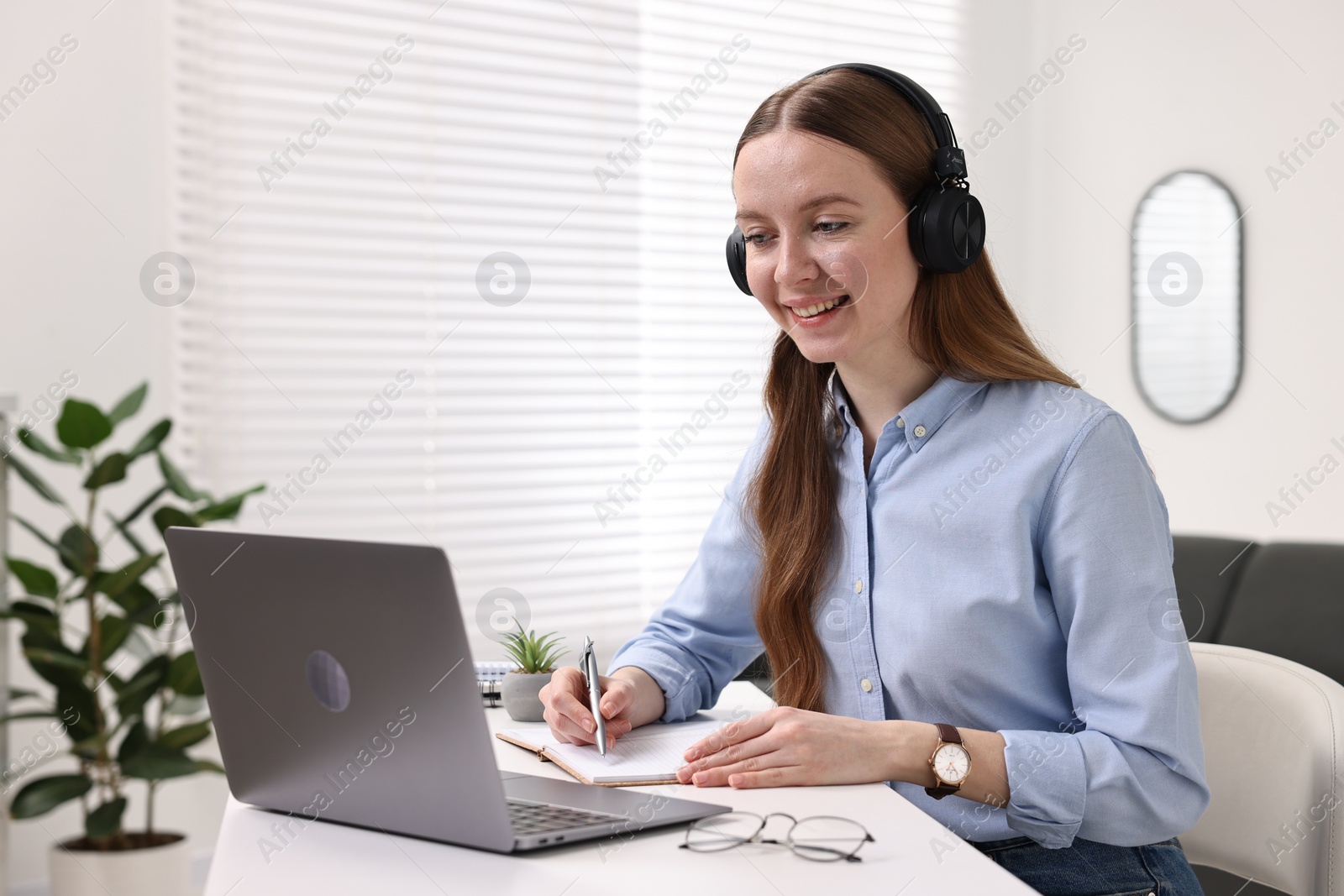 Photo of E-learning. Young woman using laptop during online lesson at white table indoors