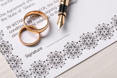 Photo of Marriage contracts, gold rings and pen on light wooden table, closeup