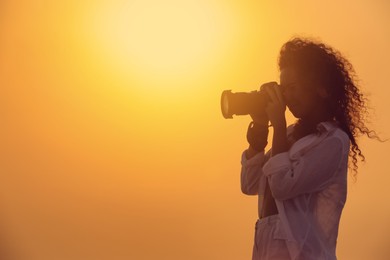 Photographer taking photo with professional camera outdoors at sunset