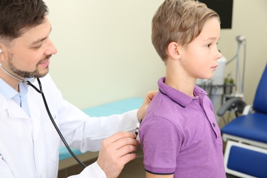 Photo of Male doctor examining little child with stethoscope in hospital