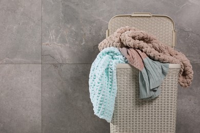 Photo of Laundry basket with clothes near grey wall. Space for text