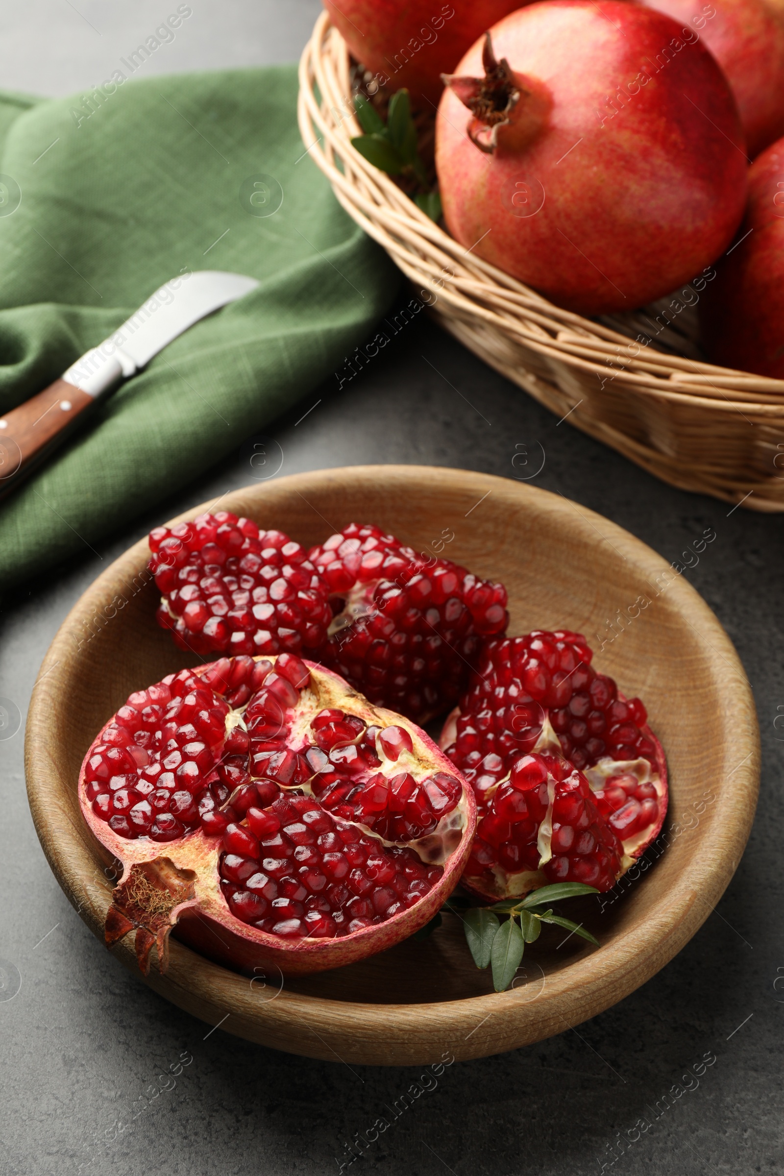 Photo of Fresh pomegranates, green leaves and knife on grey table