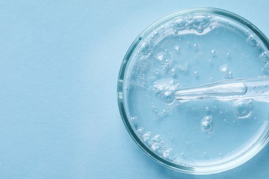 Photo of Glass pipette and petri dish with liquid on light blue background, top view. Space for text